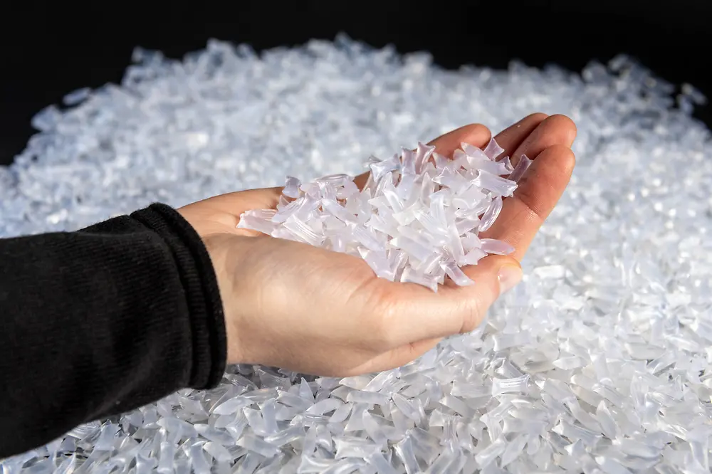 A hand holds a handful of white, semi-trasparent chubs above a big pile of the same type of chubs.