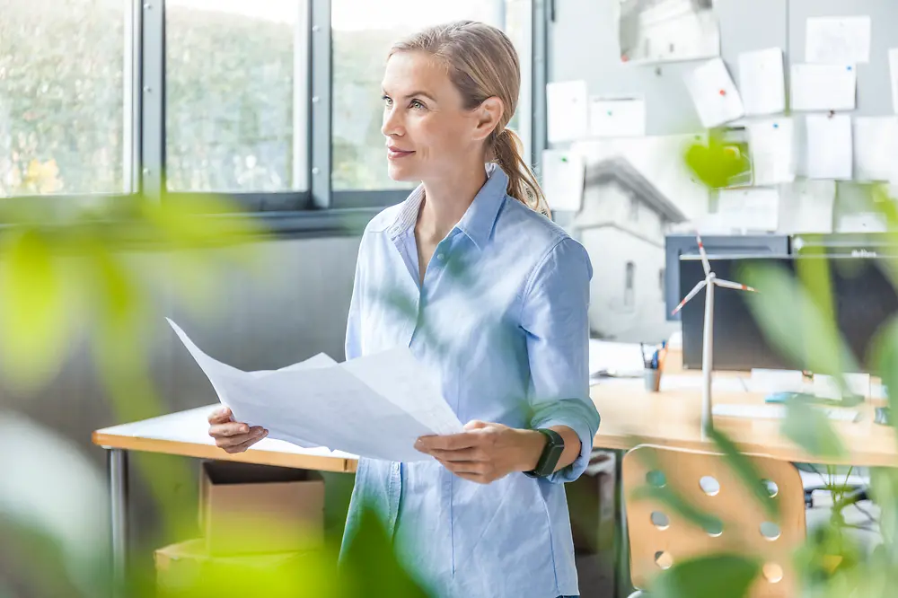 woman holding documents in an office with plant