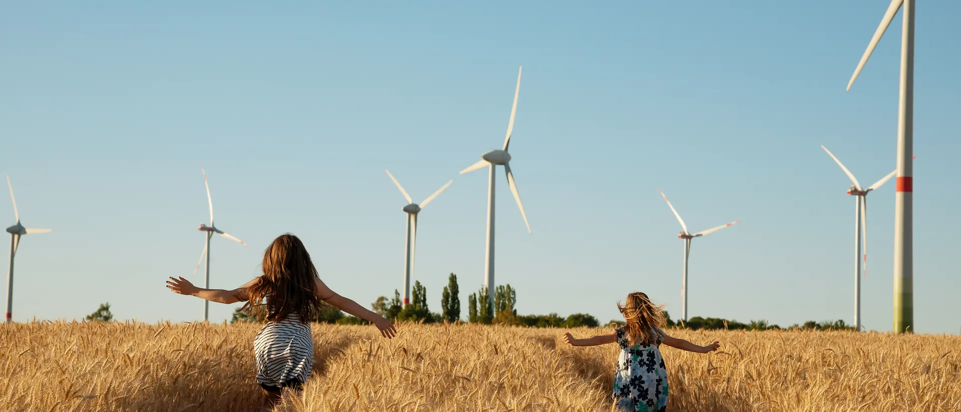 2 girls running in a cornfield with modern windmills in the background