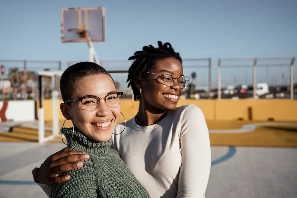 a white and black colored women that hug each other on a basketball field 