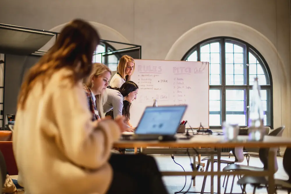 Women work on laptops in front of a flipchart.