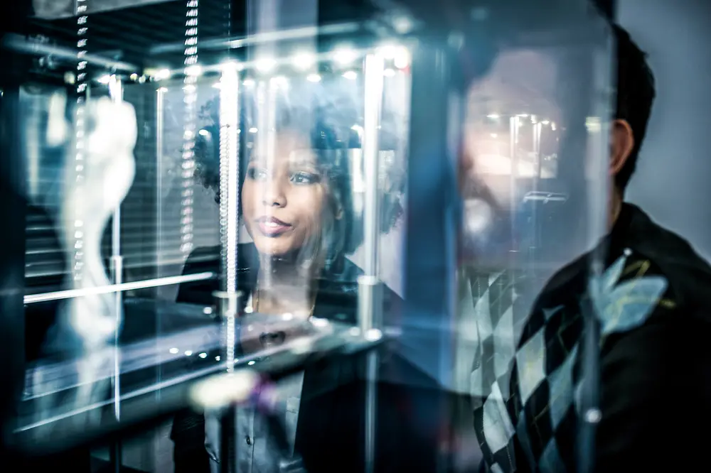 People in front of an illuminated display watching a 3D printing process.