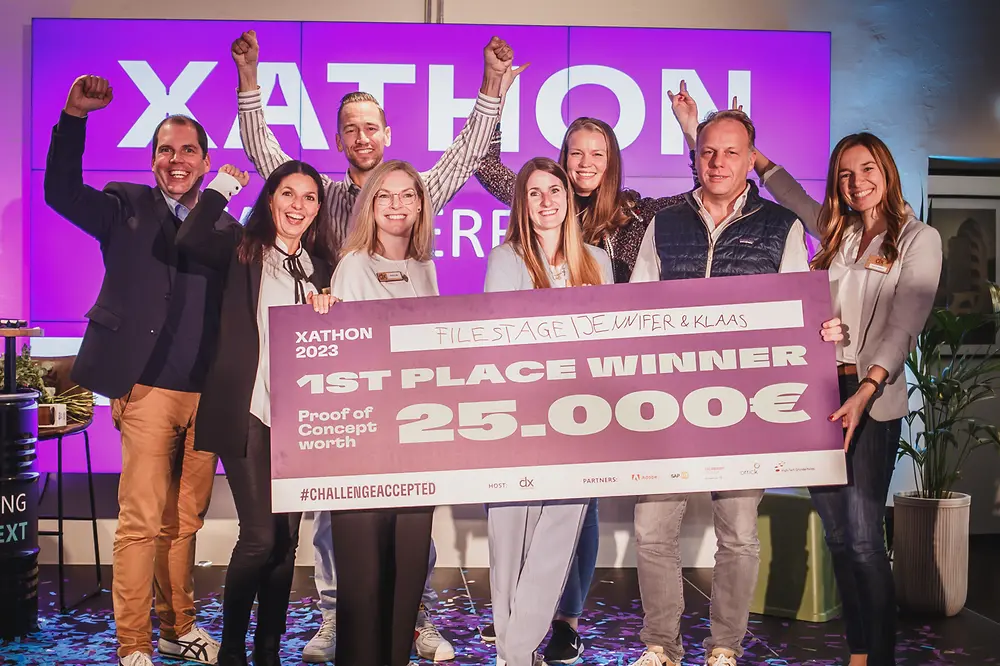 Three men and five women standing on stage cheering and holding a cheque saying 